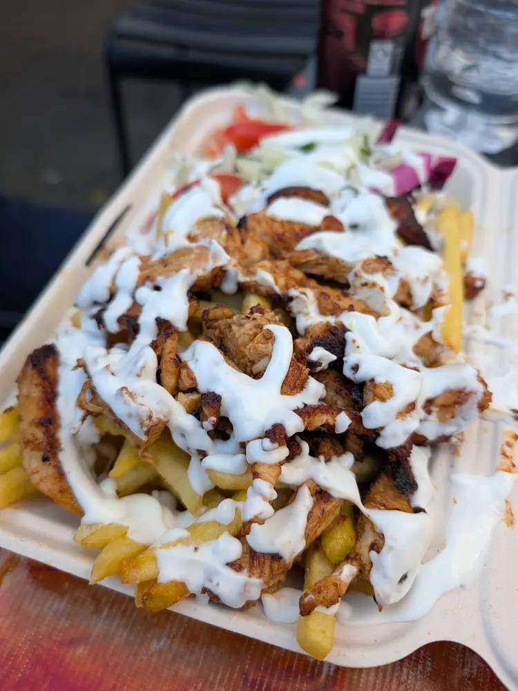 Takeaway box of grilled chicken on chips with white garlic sauce, salad and red cabbage